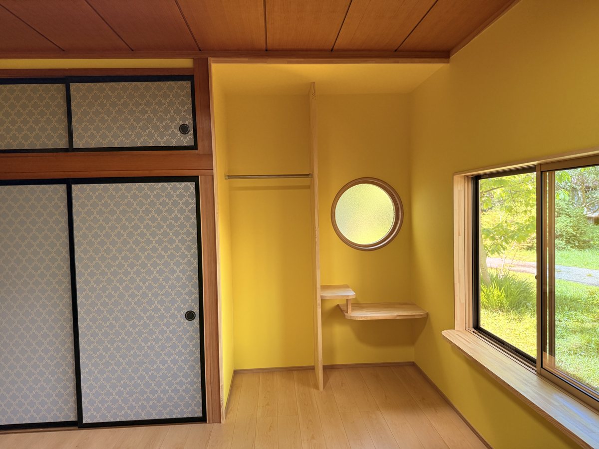 黄色い壁に丸窓と木の棚を組み合わせた、お部屋の一角
